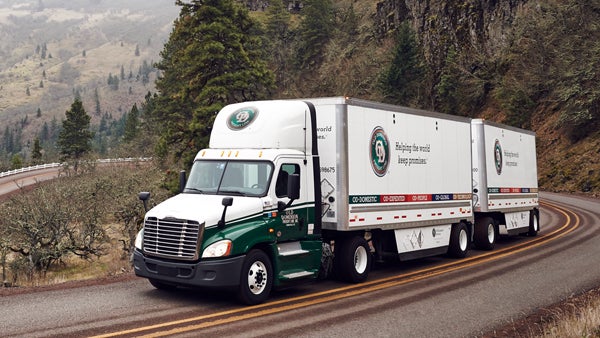 Freight truck driving on a winding road through the Oregon mountains in fall, highlighting freight shipping to Canada.