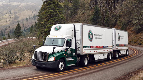 Freight truck driving on a winding road through the Oregon mountains in fall, highlighting freight shipping to Canada.